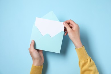 Photo of Woman taking card out of letter envelope at light blue table, top view