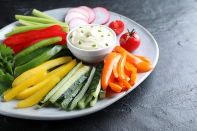 Photo of Fresh raw vegetable sticks and sauce on black table, closeup