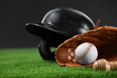 Photo of Batting helmet, leather glove and baseball ball on green grass against dark background, closeup