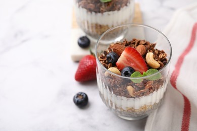 Photo of Tasty granola with berries, nuts and yogurt in glass on white marble table, closeup. Space for text