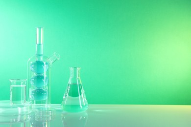 Photo of Laboratory analysis. Different glassware on table against green background, space for text