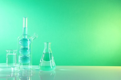 Laboratory analysis. Different glassware on table against green background, space for text