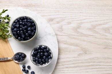 Photo of Ripe bilberries and sprigs with leaves on light wooden table, top view. Space for text