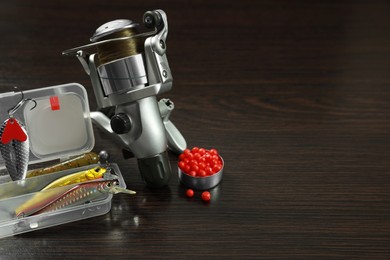 Fishing tackle. Spinning reel, bait and lures on dark wooden background, space for text