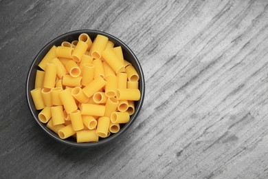 Photo of Raw rigatoni pasta in bowl on grey table, top view. Space for text