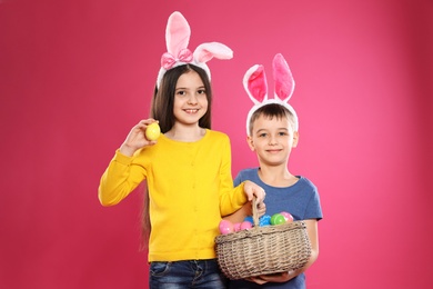 Photo of Cute children in bunny ears headbands holding basket with Easter eggs on color background