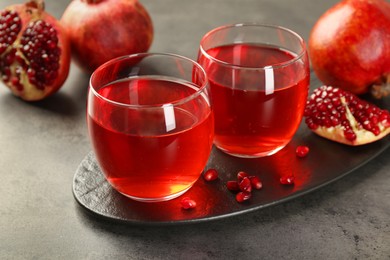 Photo of Tasty pomegranate juice in glasses and fresh fruits on grey table