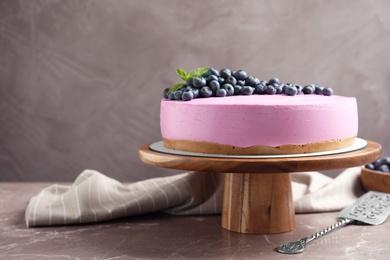 Photo of Wooden stand with tasty blueberry cake on grey table. Space for text