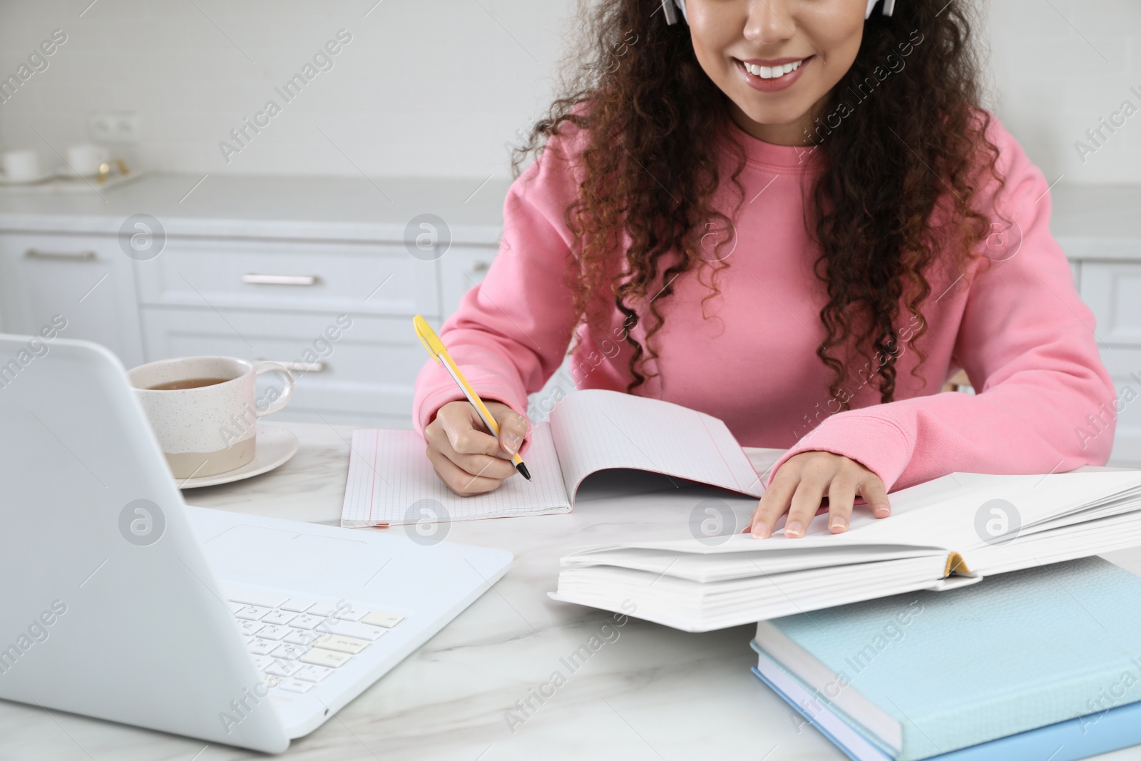 Photo of African American woman with modern laptop studying in kitchen, closeup. Distance learning