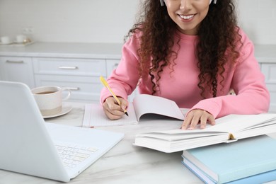 Photo of African American woman with modern laptop studying in kitchen, closeup. Distance learning