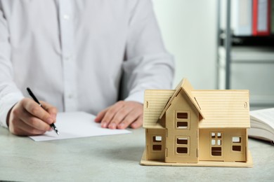 Photo of Construction and land law concepts. Man writing at white table, focus on house model