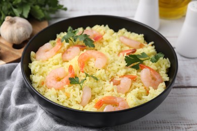 Photo of Delicious risotto with shrimps and parsley in bowl on white wooden table, closeup