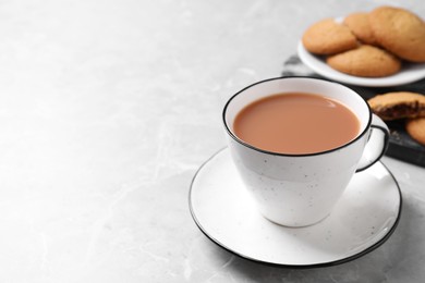 Photo of Delicious tea with milk in white cup near cookies on grey table. Space for text