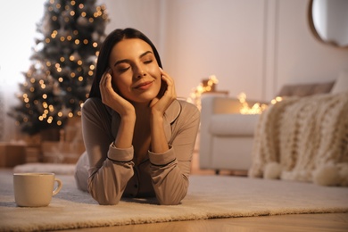 Photo of Young woman on carpet at home, space for text. Christmas celebration