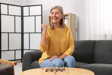 Photo of Happy senior woman enjoying winning after playing checkers at home