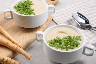 Photo of Bowls with tasty creamy soup of parsnip served on light grey table, closeup