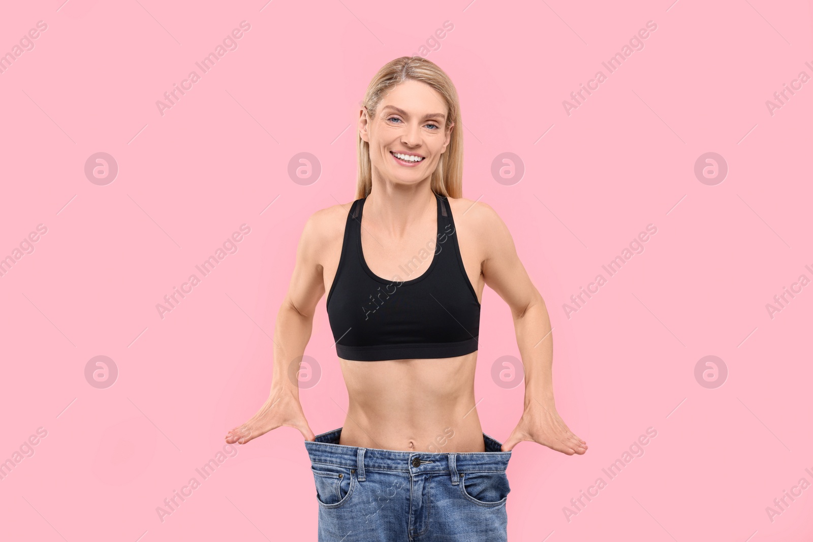 Photo of Slim woman wearing big jeans on pink background. Weight loss