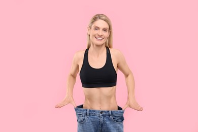 Photo of Slim woman wearing big jeans on pink background. Weight loss