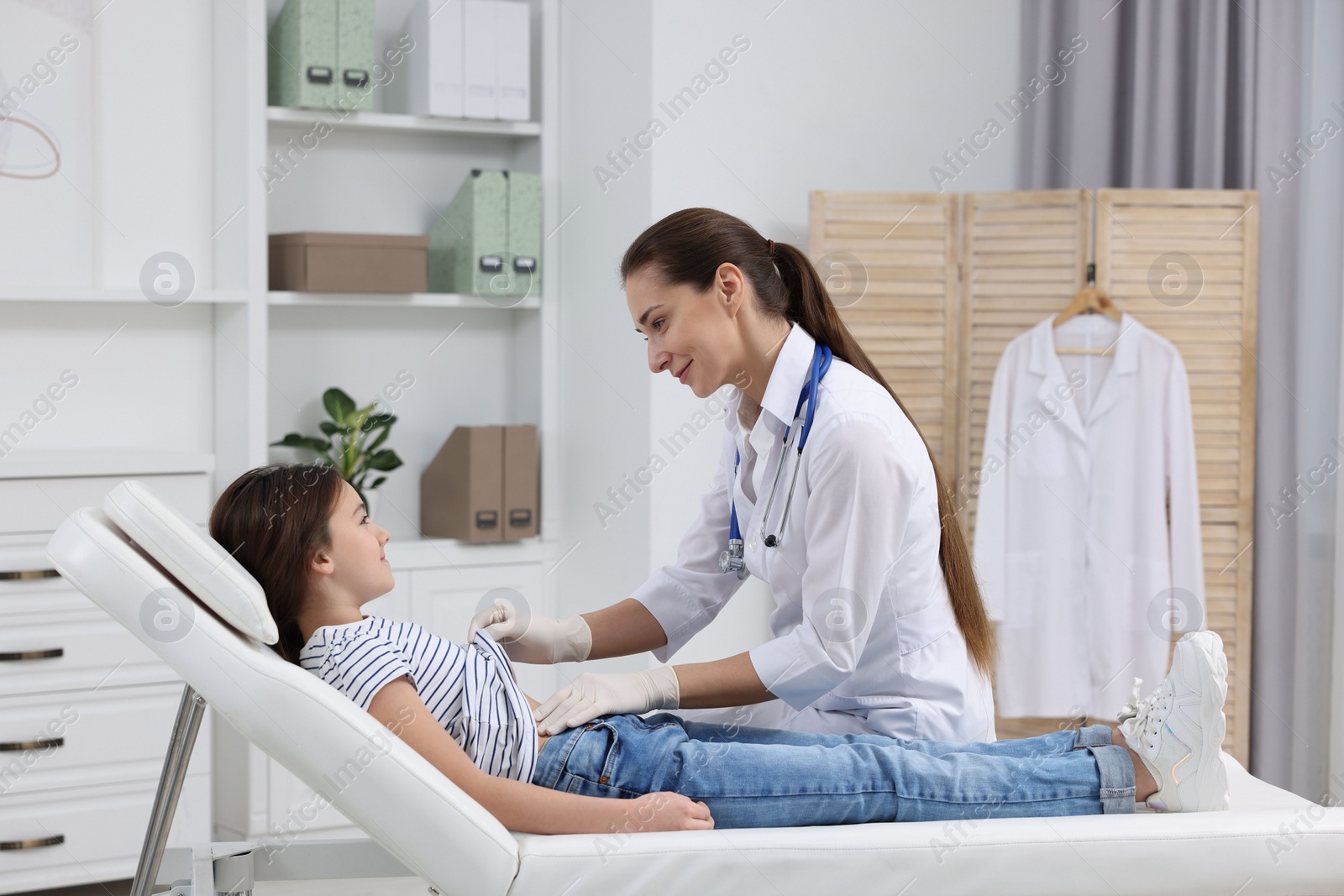 Photo of Gastroenterologist examining girl with stomach ache on couch in clinic