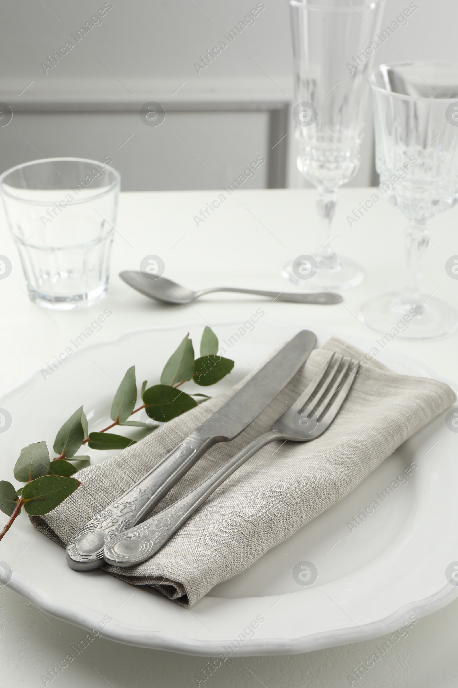 Photo of Stylish setting with cutlery, eucalyptus leaves and plate on white textured table, closeup