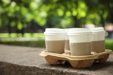 Takeaway paper coffee cups with plastic lids and sleeves in cardboard holder outdoors, space for text