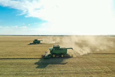 Photo of Beautiful aerial view of modern combine harvesters working in field on sunny day. Agriculture industry