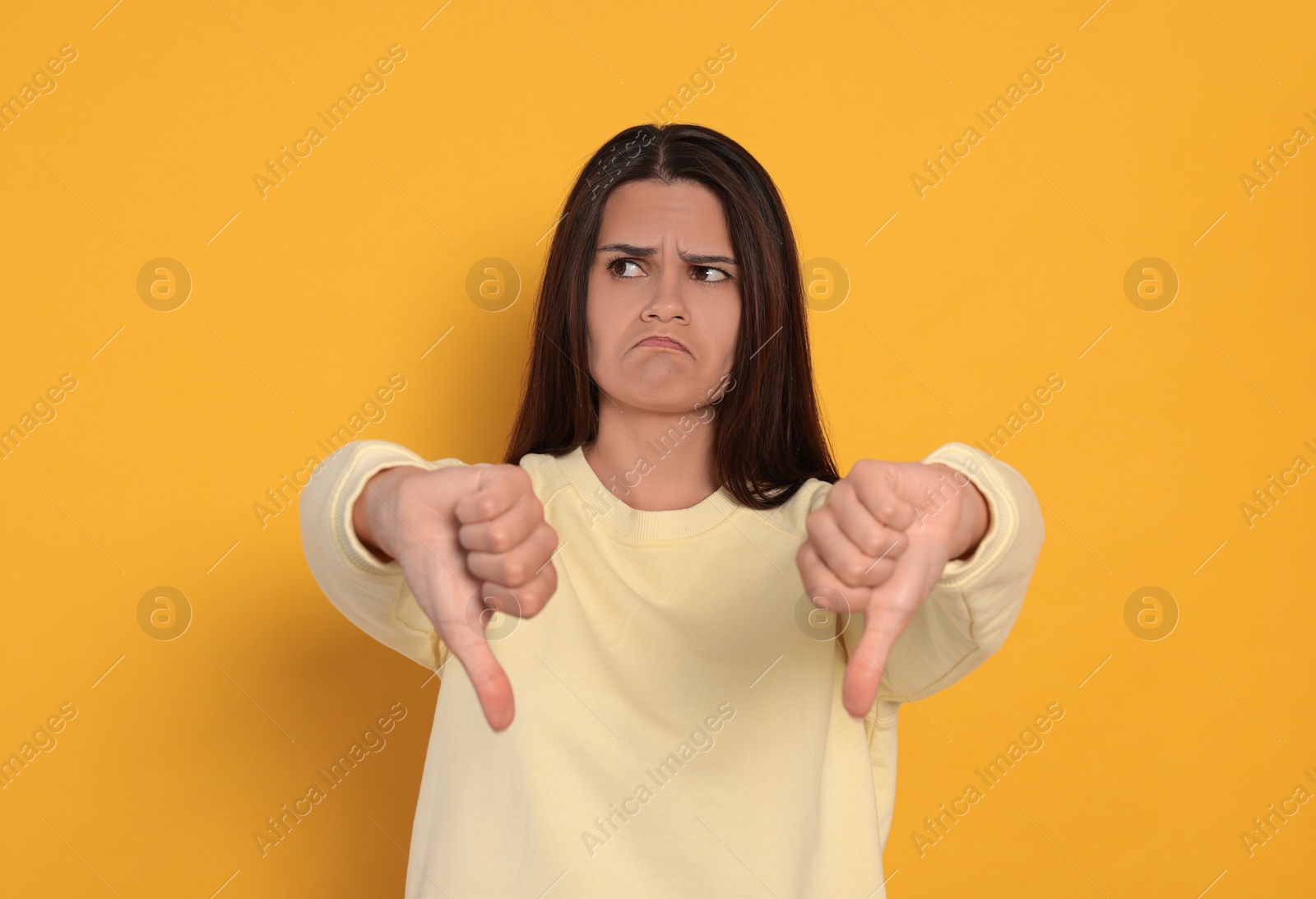 Photo of Young woman showing thumbs down on orange background