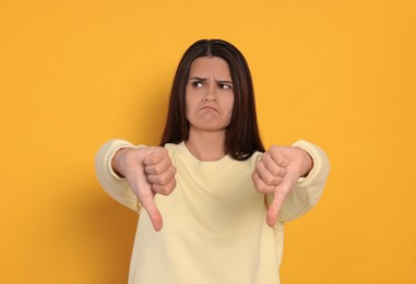 Young woman showing thumbs down on orange background