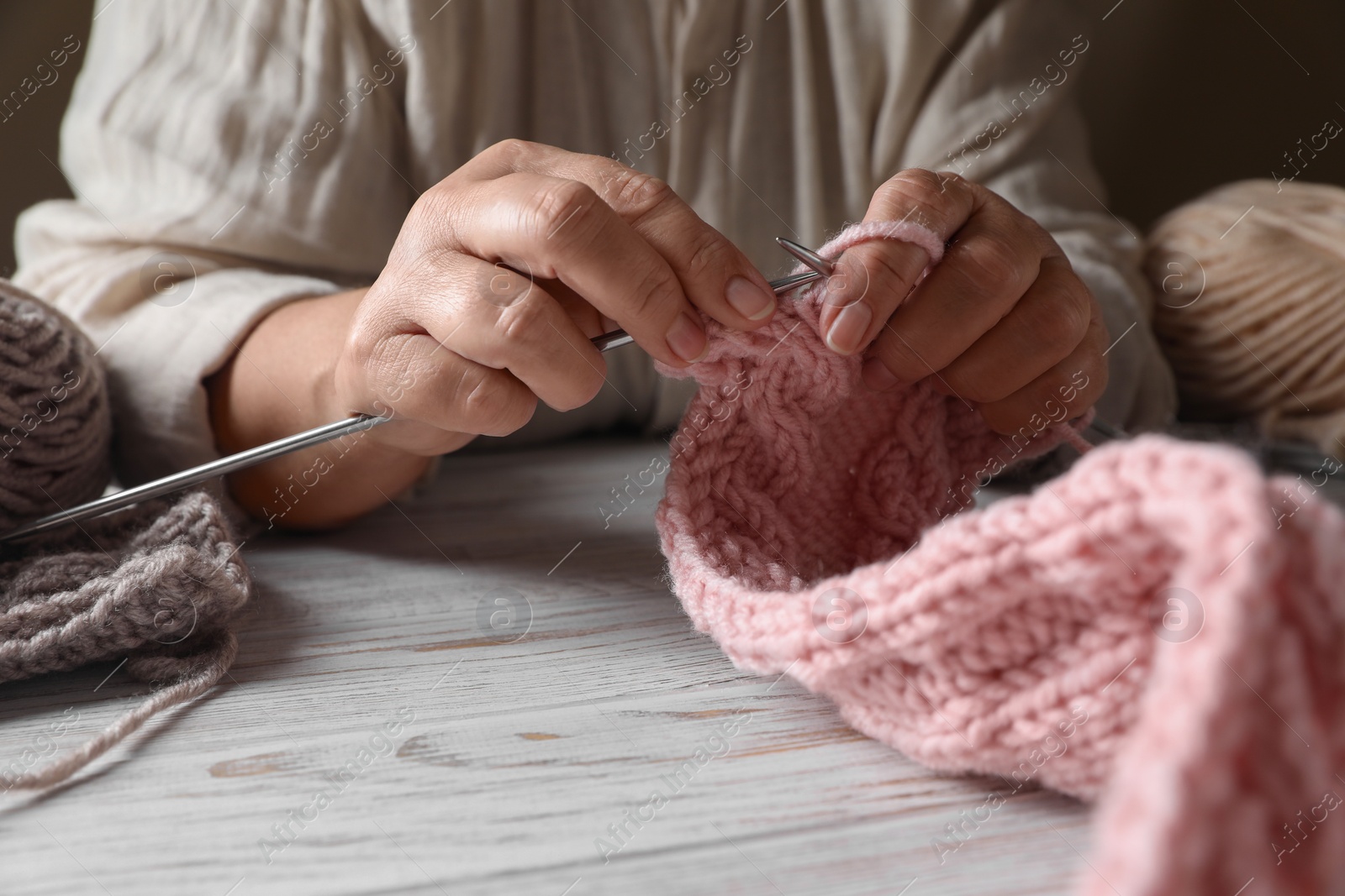 Photo of Woman knitting at white wooden table, closeup. Creative hobby