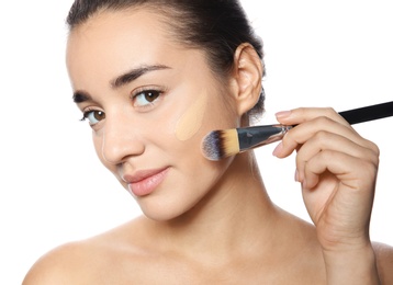 Young woman applying foundation on her face against white background