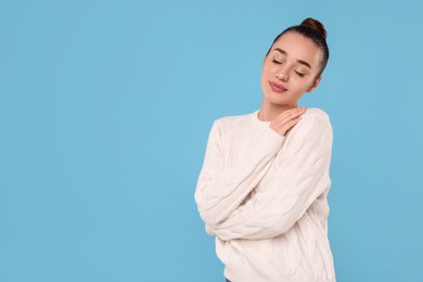 Photo of Beautiful young woman in stylish warm sweater on light blue background, space for text
