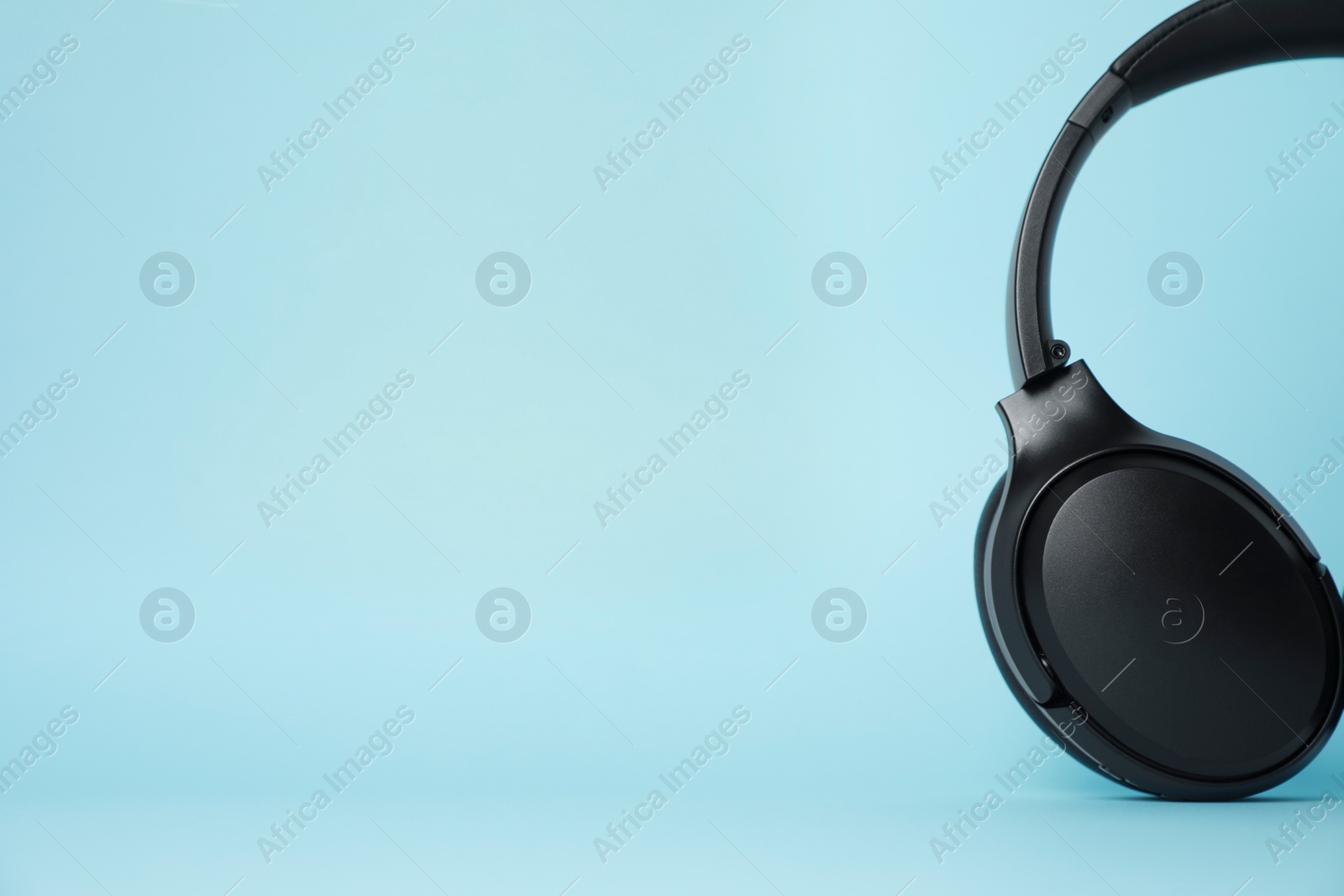 Photo of Modern wireless headphones on light blue background. Space for text