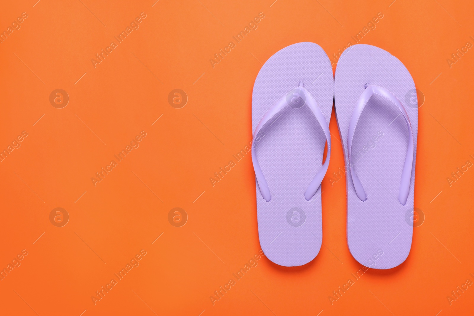 Photo of Stylish violet flip flops on orange background, top view. Space for text