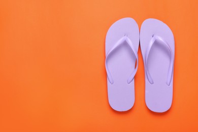 Stylish violet flip flops on orange background, top view. Space for text