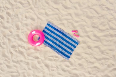 Image of Striped beach towel, flip flops and swim ring on sand, aerial view