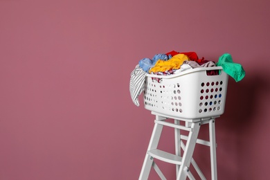 Photo of Laundry basket with dirty clothes on step ladder against color background