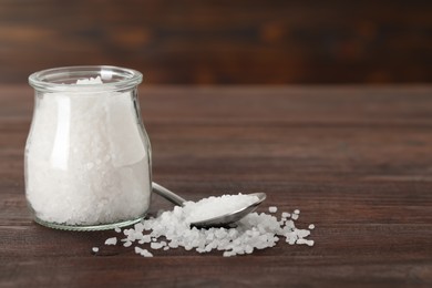 Photo of Natural sea salt, glass jar and spoon on wooden table. Space for text