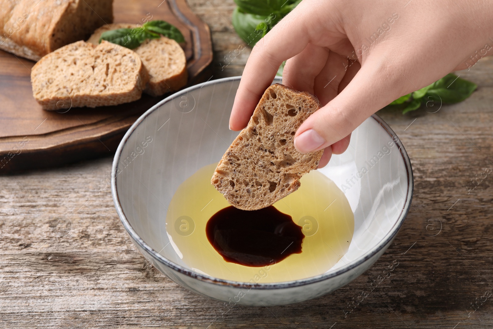 Photo of Woman dipping piece of bread into balsamic vinegar with oil at wooden table, closeup