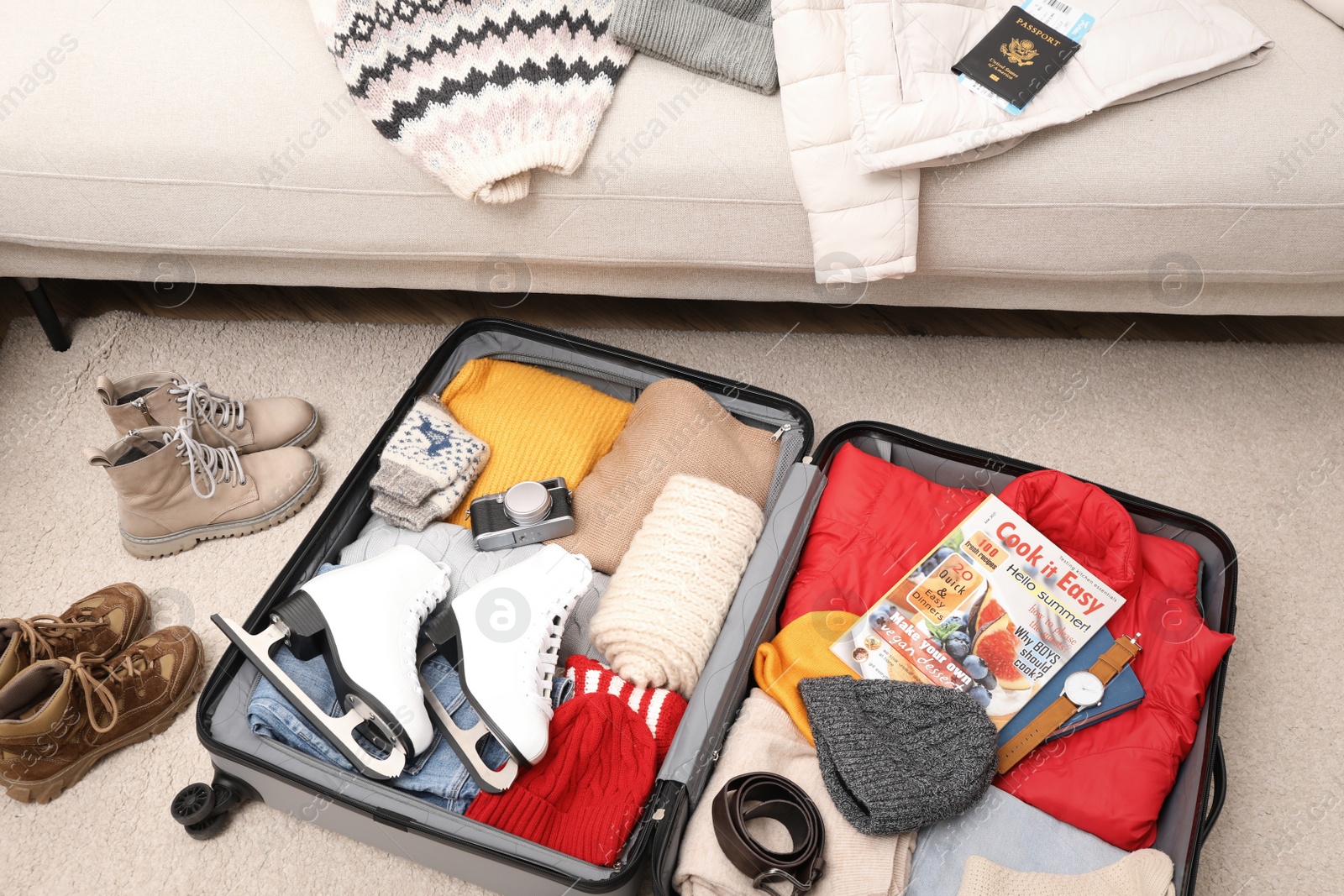 Photo of Open suitcase with warm clothes, accessories and shoes near sofa indoors