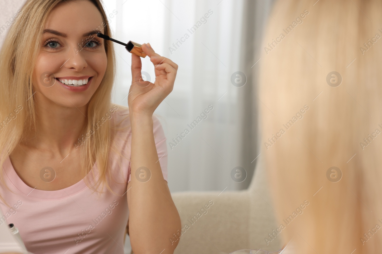 Photo of Beautiful woman applying mascara near mirror at home