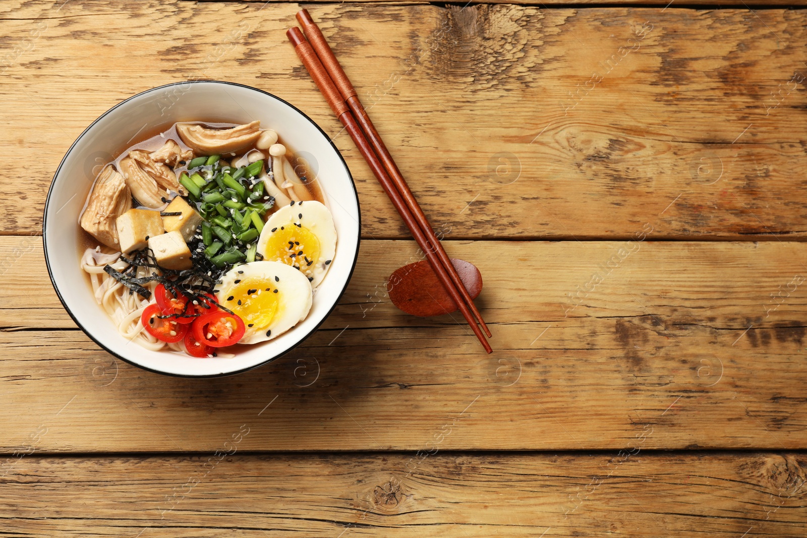 Photo of Noodle soup. Bowl of delicious ramen and chopsticks on wooden table, top view. Space for text