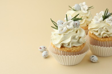 Tasty Easter cupcakes with vanilla cream and candies on beige background, space for text