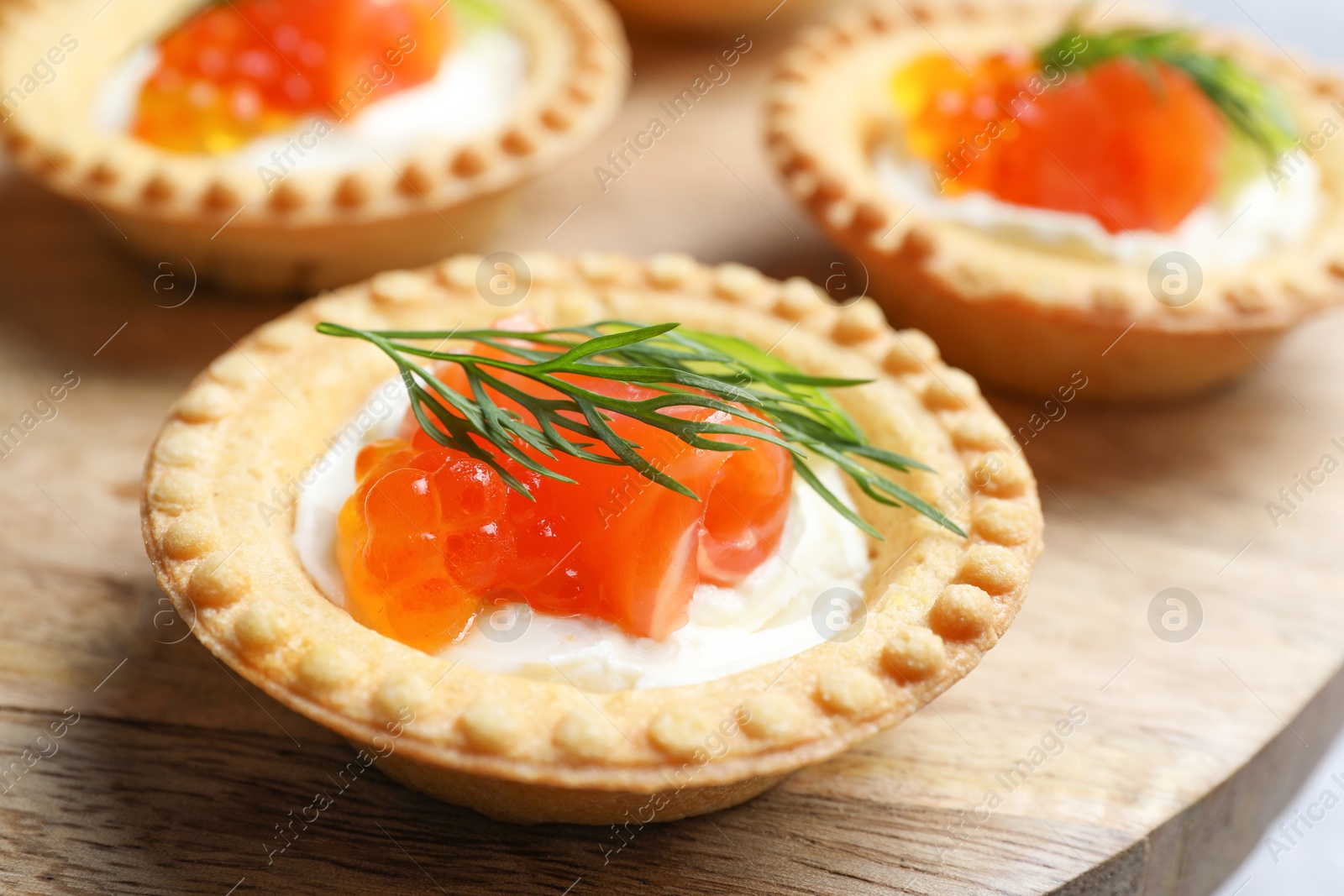 Photo of Delicious canapes with salmon and red caviar on wooden board, closeup