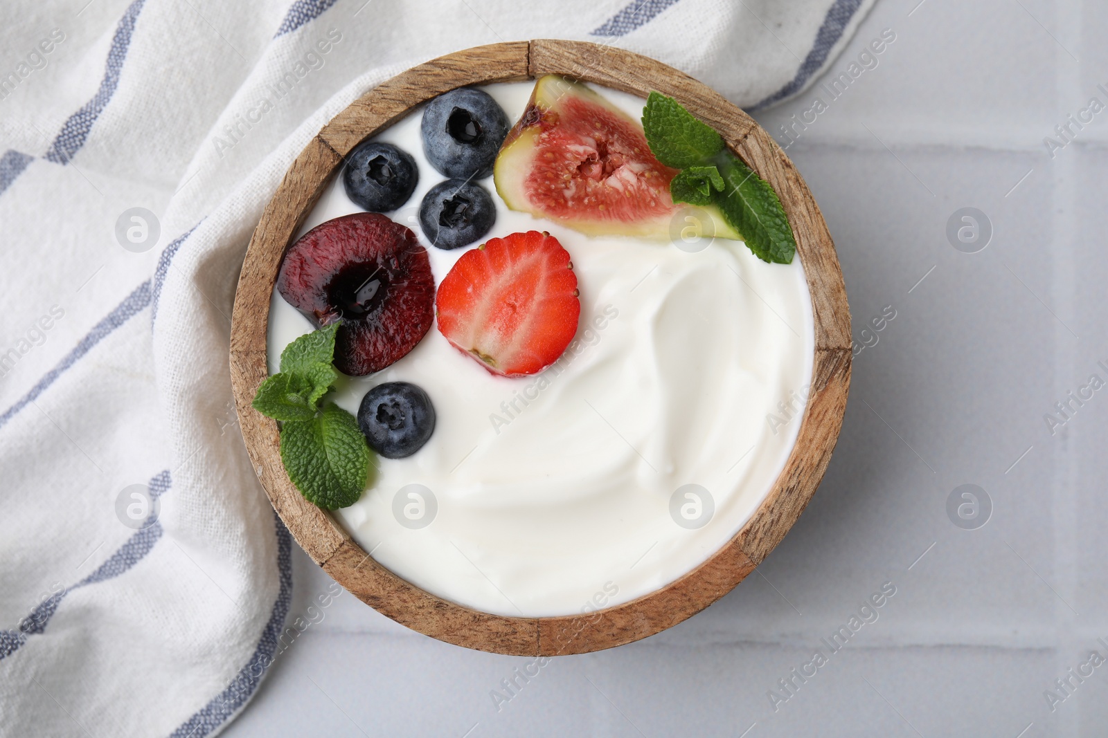 Photo of Bowl with yogurt, berries, fruits and mint on white tiled table, top view