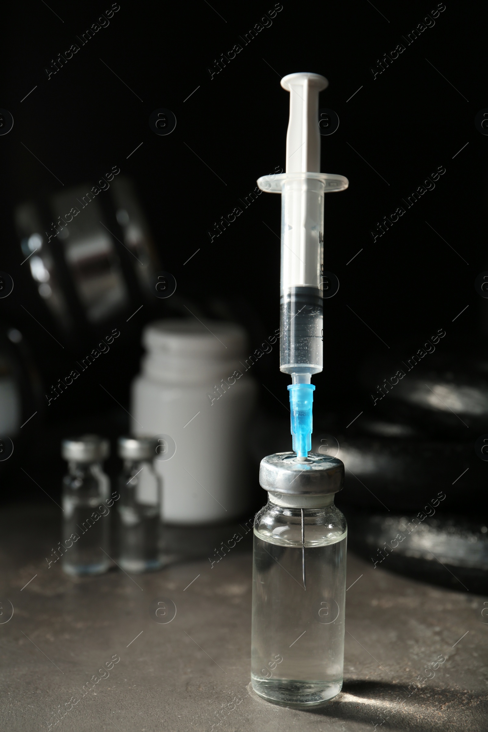 Photo of Vial and syringe with drug near sports equipment on grey table, space for text. Doping control