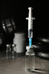 Vial and syringe with drug near sports equipment on grey table, space for text. Doping control