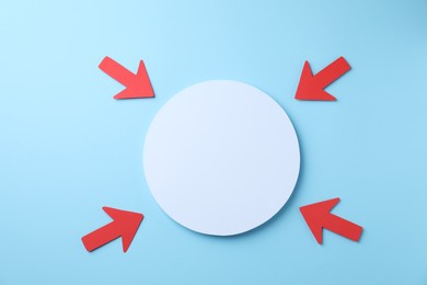 Photo of Red paper arrows and white circle on light blue background, flat lay. Space for text