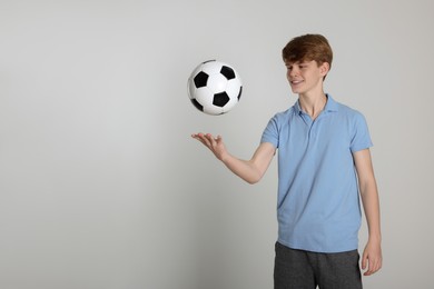 Photo of Teenage boy playing with soccer ball on light grey background. Space for text