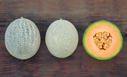 Whole and cut fresh ripe melons on wooden table, flat lay