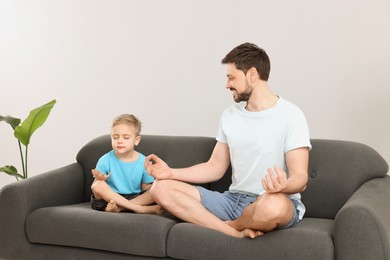 Father with son meditating together on sofa at home